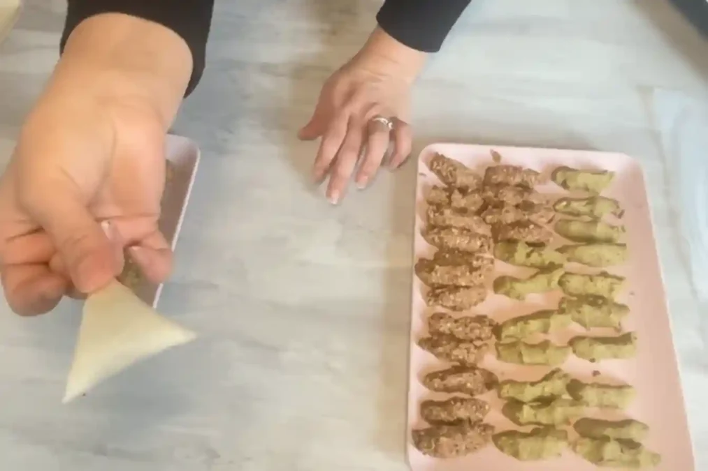 Façonnage d’un briouate au poulet en triangle, avec des rouleaux déjà préparés sur un plateau